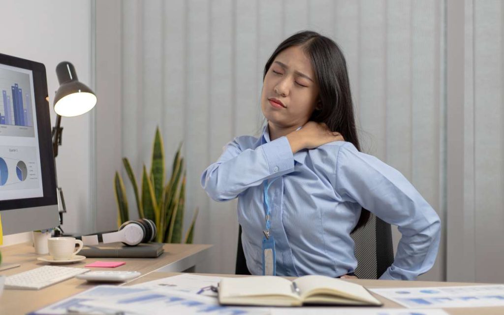 Una mujer con dolor de espalda por estar mucho tiempo sentada con alta carga de trabajo 
